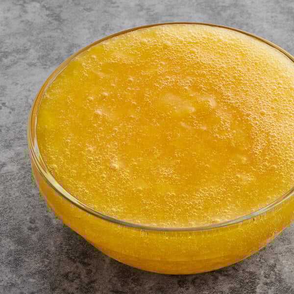 A bowl of Oregon Fruit In Hand Original Diced Mango in yellow liquid on a gray surface.