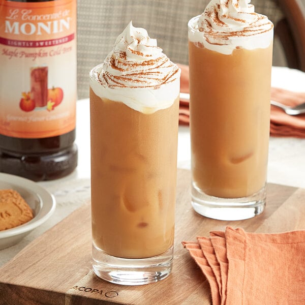 Two glasses of Monin Maple Pumpkin cold brew coffee on a table in a coffee shop.