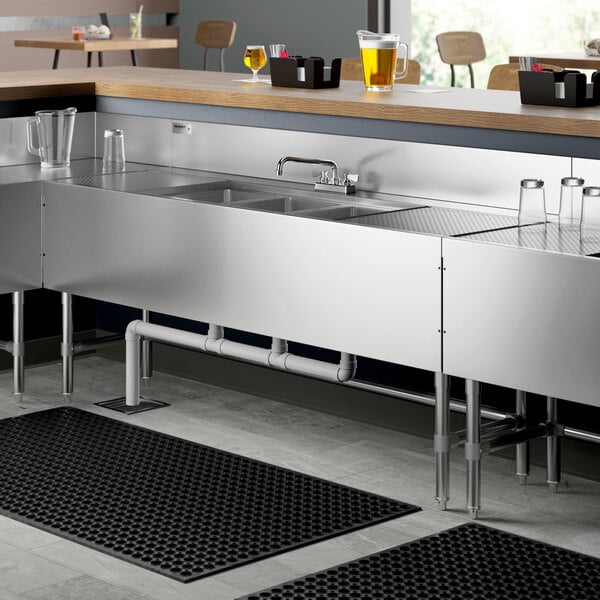 A Regency stainless steel underbar sink with (2) drainboards and faucet on a counter.