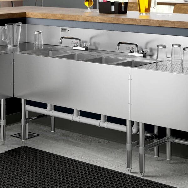 A Regency stainless steel underbar sink with two faucets over four bowls.
