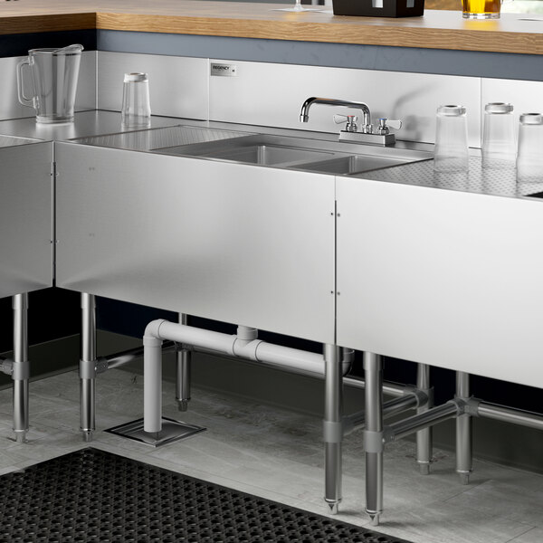 A Regency stainless steel underbar sink with two bowls, a left drainboard, and a faucet.