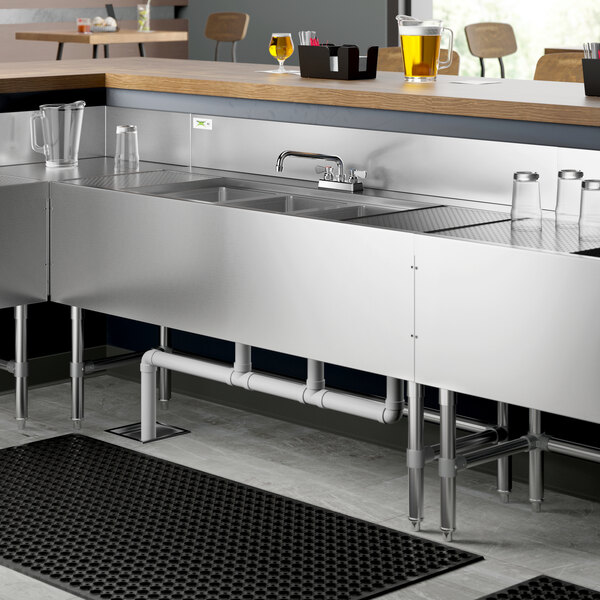 A Regency stainless steel underbar sink with (2) 12" drainboards installed on a counter.