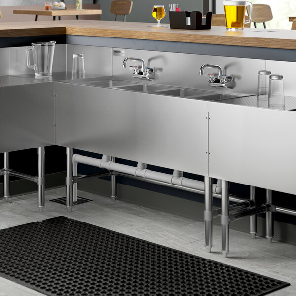 A Regency stainless steel underbar sink with four bowls and two faucets on a counter.