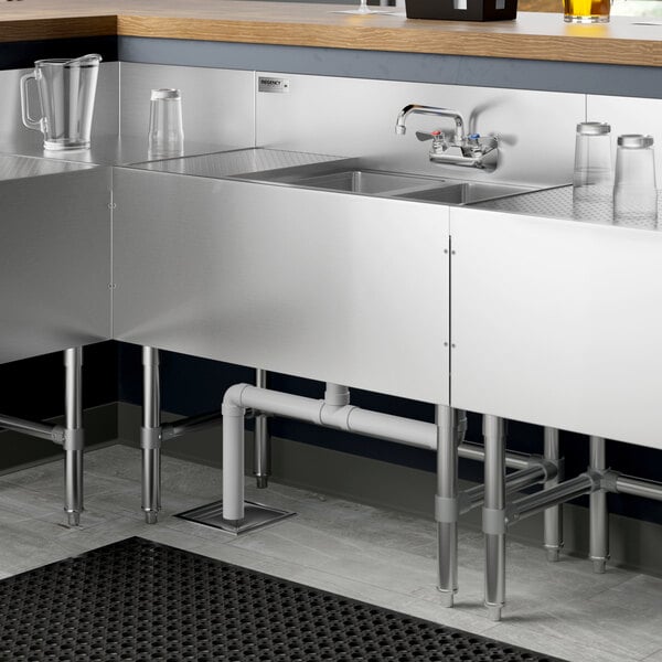 A Regency stainless steel underbar sink with two bowls, a drainboard, and a faucet.