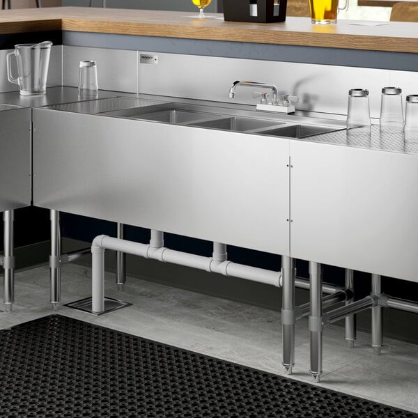 A Regency stainless steel underbar sink with three bowls, a left drainboard, and a faucet on a counter.