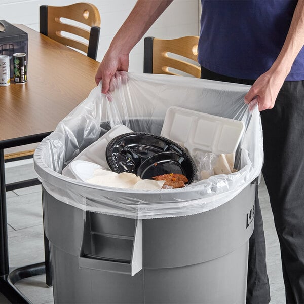 A person putting a EcoStrong Plus clear plastic bag into a trash can.