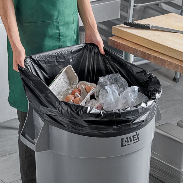 A woman holding a black EcoStrong Plus trash bag with food in it.