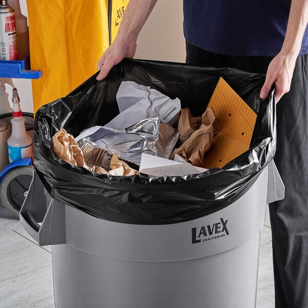 A man holding a trash can full of paper and other objects.