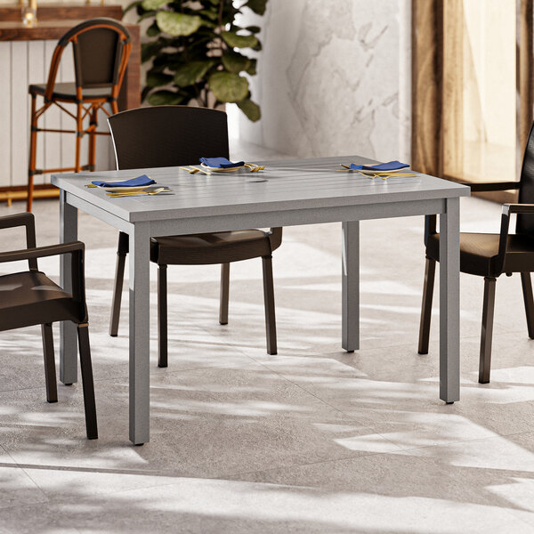 A Grosfillex Sigma volcanic black aluminum dining table with chairs underneath.