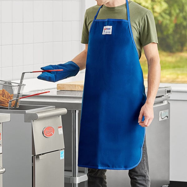 A man wearing a blue Tucker Safety Products Burnguard apron cooking in a professional kitchen.
