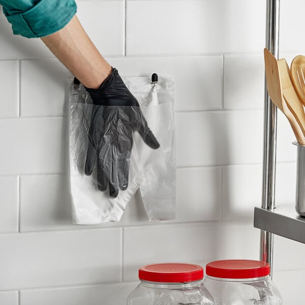 A stainless steel Pak-Sher wall mount glove dispenser holding a gloved hand from a plastic bag.