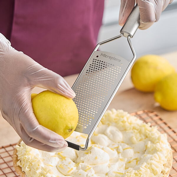 A stainless steel paddle style fine grater being used to zest a lemon.