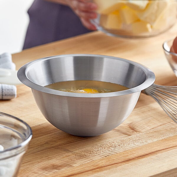 A woman using a Matfer Bourgeat stainless steel mixing bowl to whisk liquid with an egg yolk.