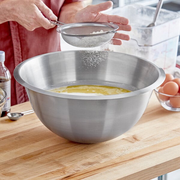 A person pouring flour into a Matfer Bourgeat stainless steel mixing bowl.