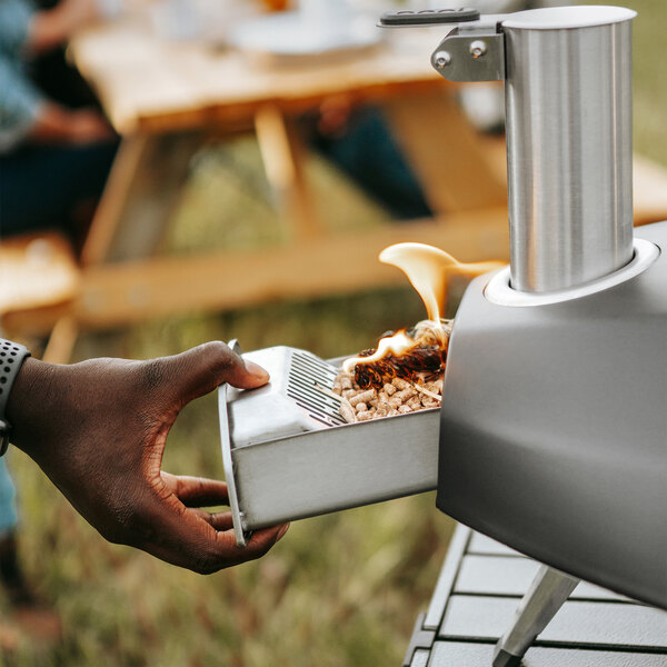 A hand using the Ooni Fyra pizza oven to cook food over a flame.