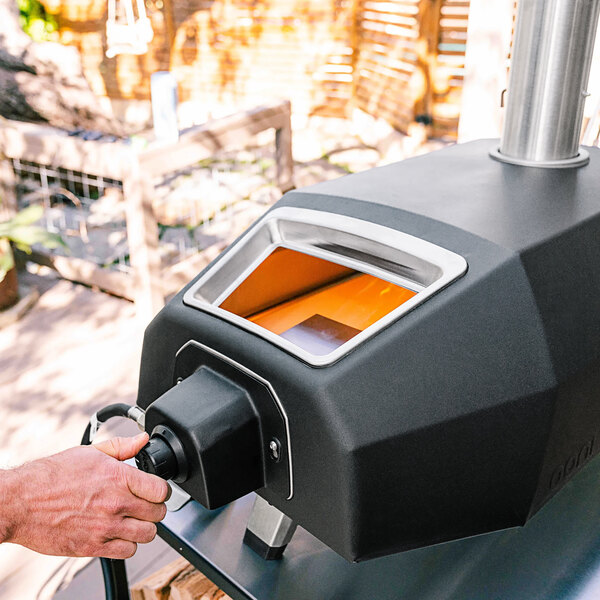 A hand using a black and silver device to turn on a gas burner.