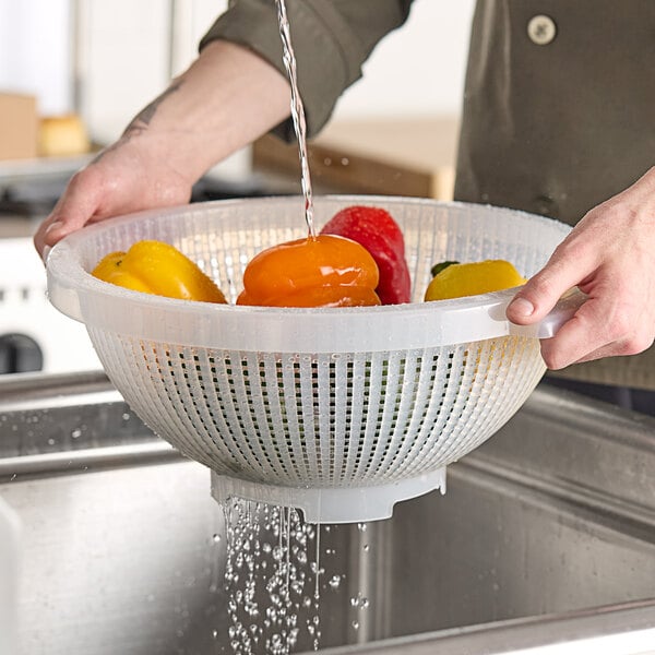 A person washing yellow peppers in a Giganplast colander.