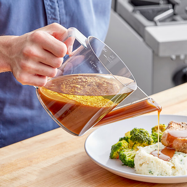 A person using a Westmark Fat Separator to pour brown liquid onto a plate of food.