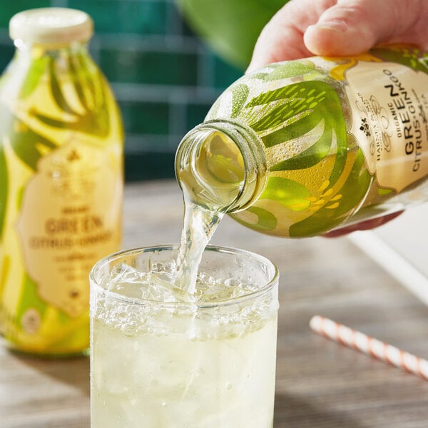 A hand pouring Harney & Sons Organic Citrus and Ginkgo Green Iced Tea from a glass pitcher into a glass.