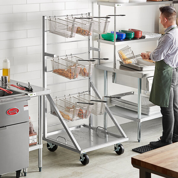 A man using an Assure Parts mobile fryer basket rack in a professional kitchen.