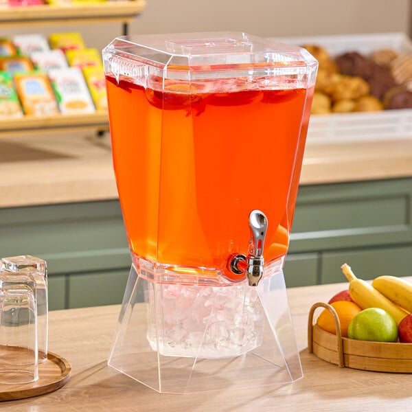 A clear acrylic beverage dispenser with a spigot, filled with red drink and ice in a separate chamber at the bottom.