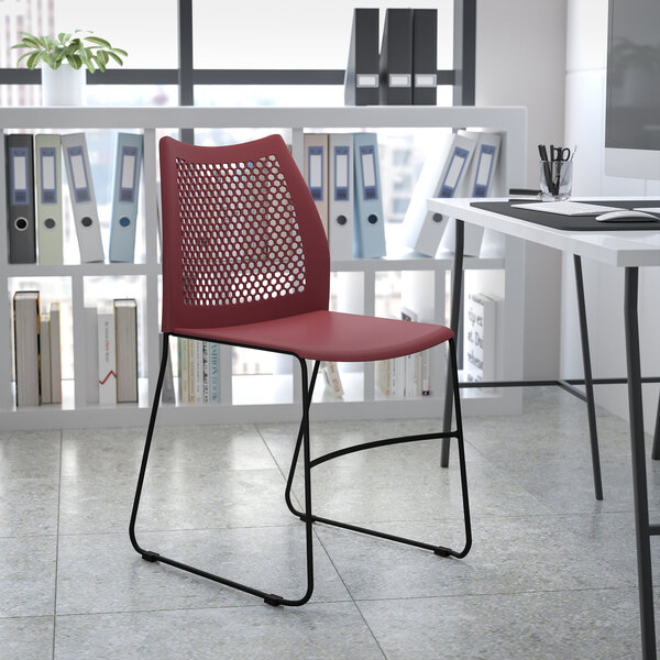A Flash Furniture burgundy stacking chair with a black sled base in a room with a white table and shelves.
