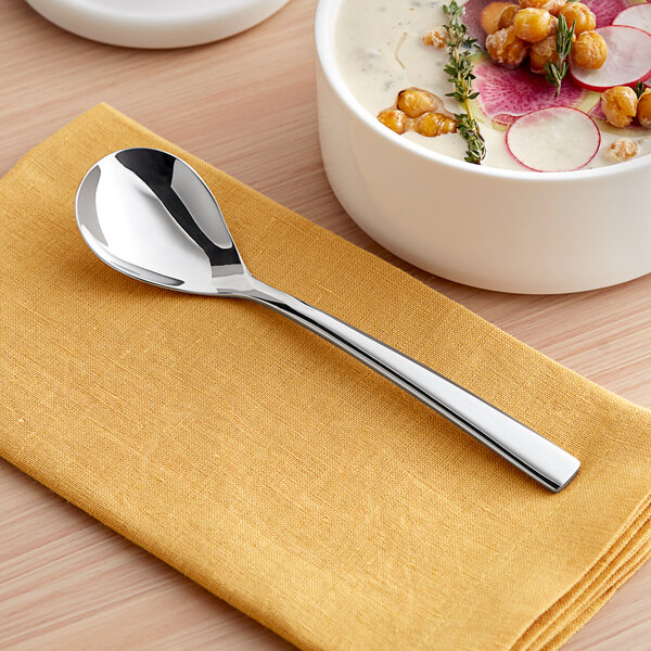 A bowl of chickpea and vegetable soup with an Acopa Lore stainless steel bouillon spoon next to it.