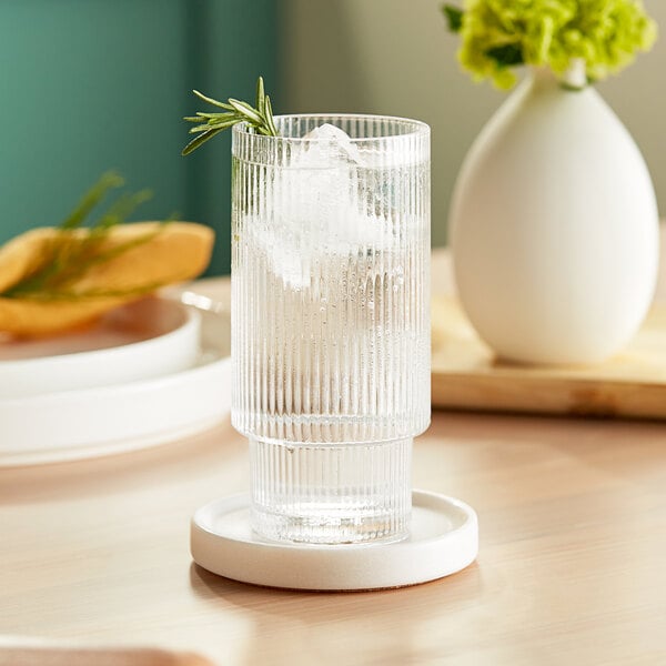 A Acopa Lore highball glass of water with ice and a sprig of rosemary on a coaster.