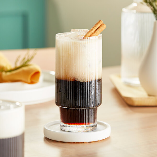 A Acopa Lore highball glass filled with a brown drink with ice and a straw.
