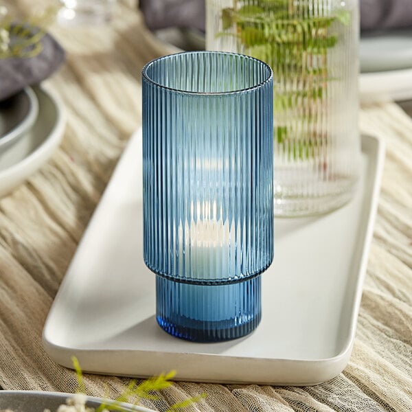 A blue glass Acopa Lore tealight holder on a white tray.