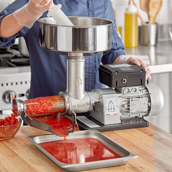 A person pouring red sauce into a Tre Spade Electric Tomato Mill.