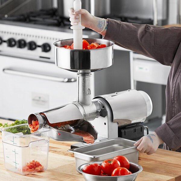 A woman using a Tre Spade electric tomato mill to process tomatoes on a counter.