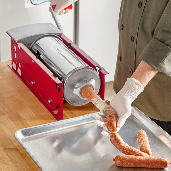 A person using a Tre Spade manual sausage stuffer to make sausages on a metal counter.