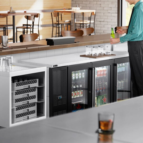 A man opening a beer while standing at a Perlick stainless steel back bar refrigerator.