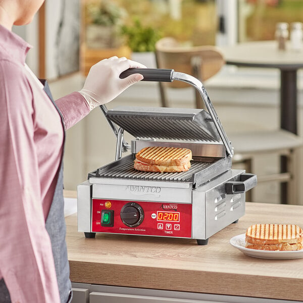 A person using an Avantco commercial Panini grill to make a sandwich.