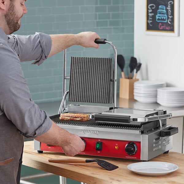 A man cooking food on an Avantco commercial panini grill.