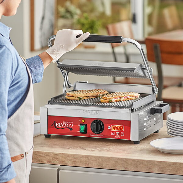 A woman using an Avantco commercial panini grill to cook a sandwich.