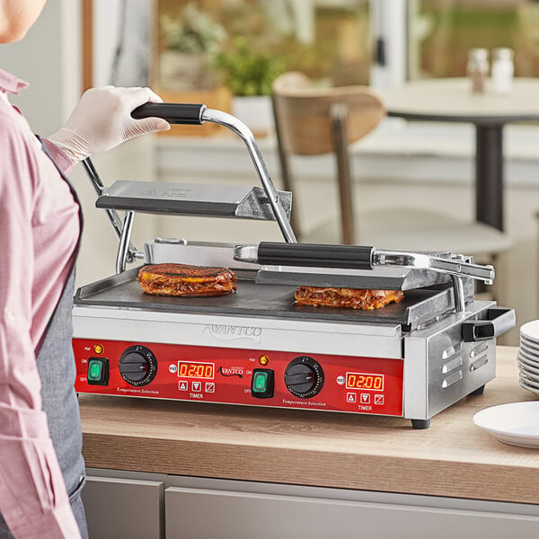 A person cooking a sandwich on an Avantco commercial panini grill.