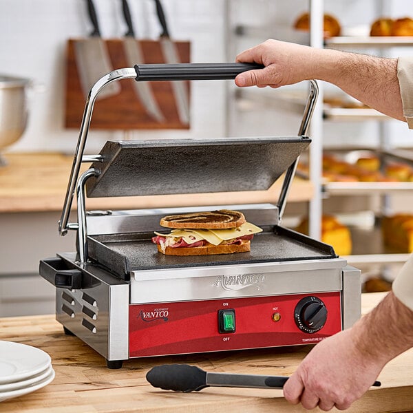 A person cooking a sandwich on an Avantco commercial panini grill.