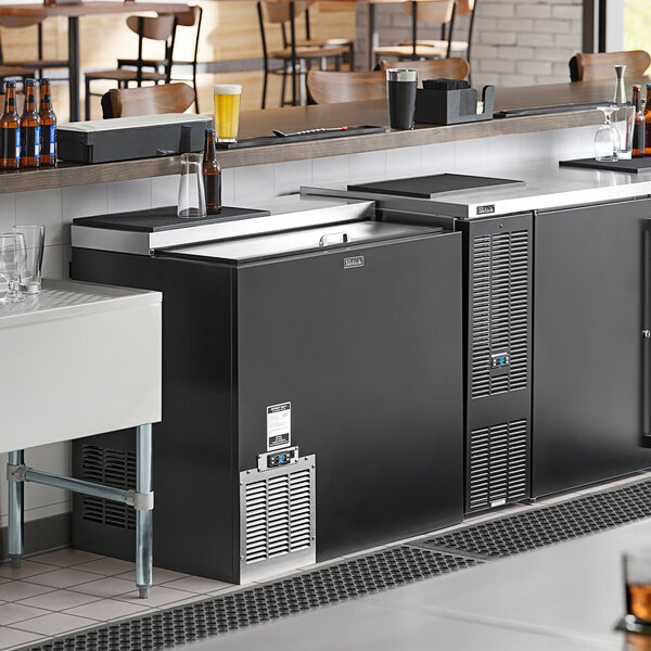 A Perlick black glass froster on a bar counter with beer bottles inside.