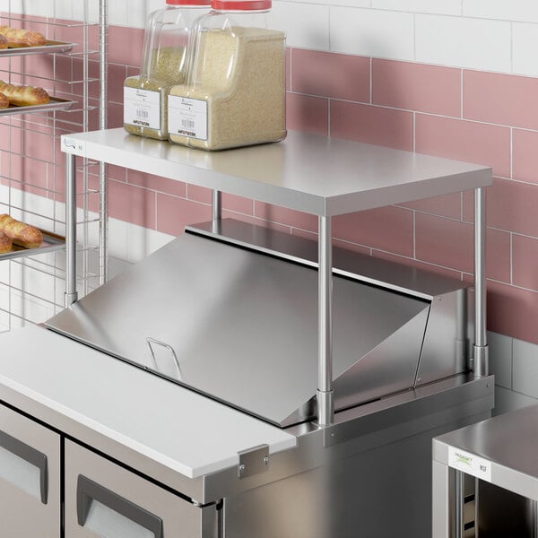 An Avantco stainless steel single deck overshelf on a counter over food shelves.