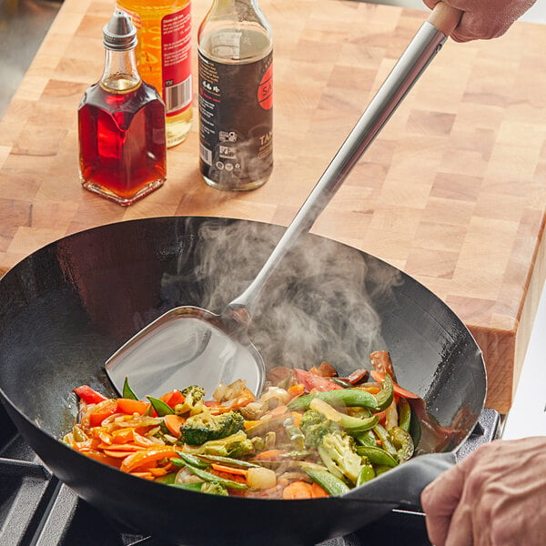 A person using an Emperor's Select wok spatula to stir food in a wok.