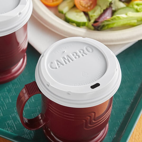 A white Cambro Sip Through Lid on a red and white Cambro insulated mug.