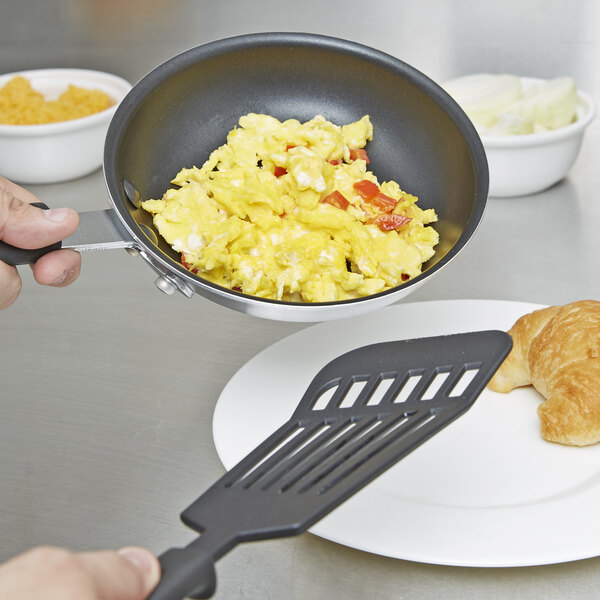 A person holding a Carlisle fry pan with scrambled eggs and tomatoes.