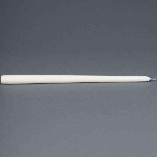 An ivory Will & Baumer taper candle in a white tube on a gray surface.