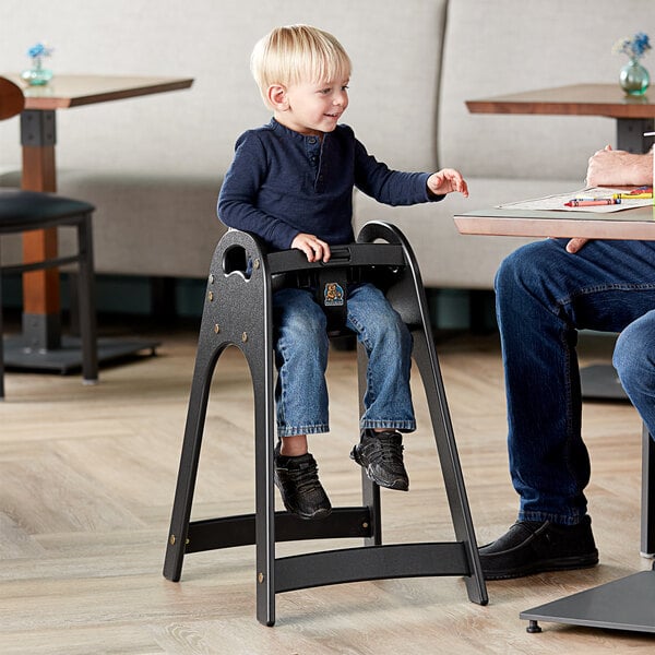 A child sitting in a black Koala Kare high chair at a table.