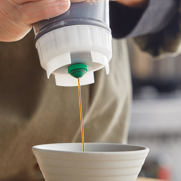 A hand using a San Jamar green valve to pour liquid into a bowl.