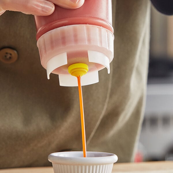 A San Jamar EZ-KLEEN 16 oz. sauce bottle with a medium valve dispensing sauce into a small white cup.