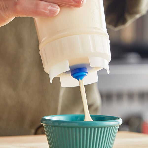 A plastic sauce bottle with a large valve dispensing a creamy liquid into a blue bowl.