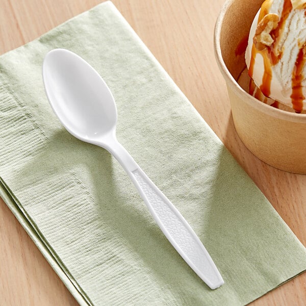 A white Choice plastic teaspoon on a napkin next to a cup of ice cream.